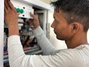 Kỹ thuật viên đang đấu nối, hiệu chỉnh thiết bị có nút nhấn xanh bên trong tủ điện cầu dao đang mở